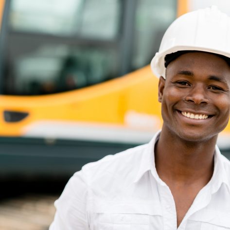 Construction worker with machines at the background looking happy